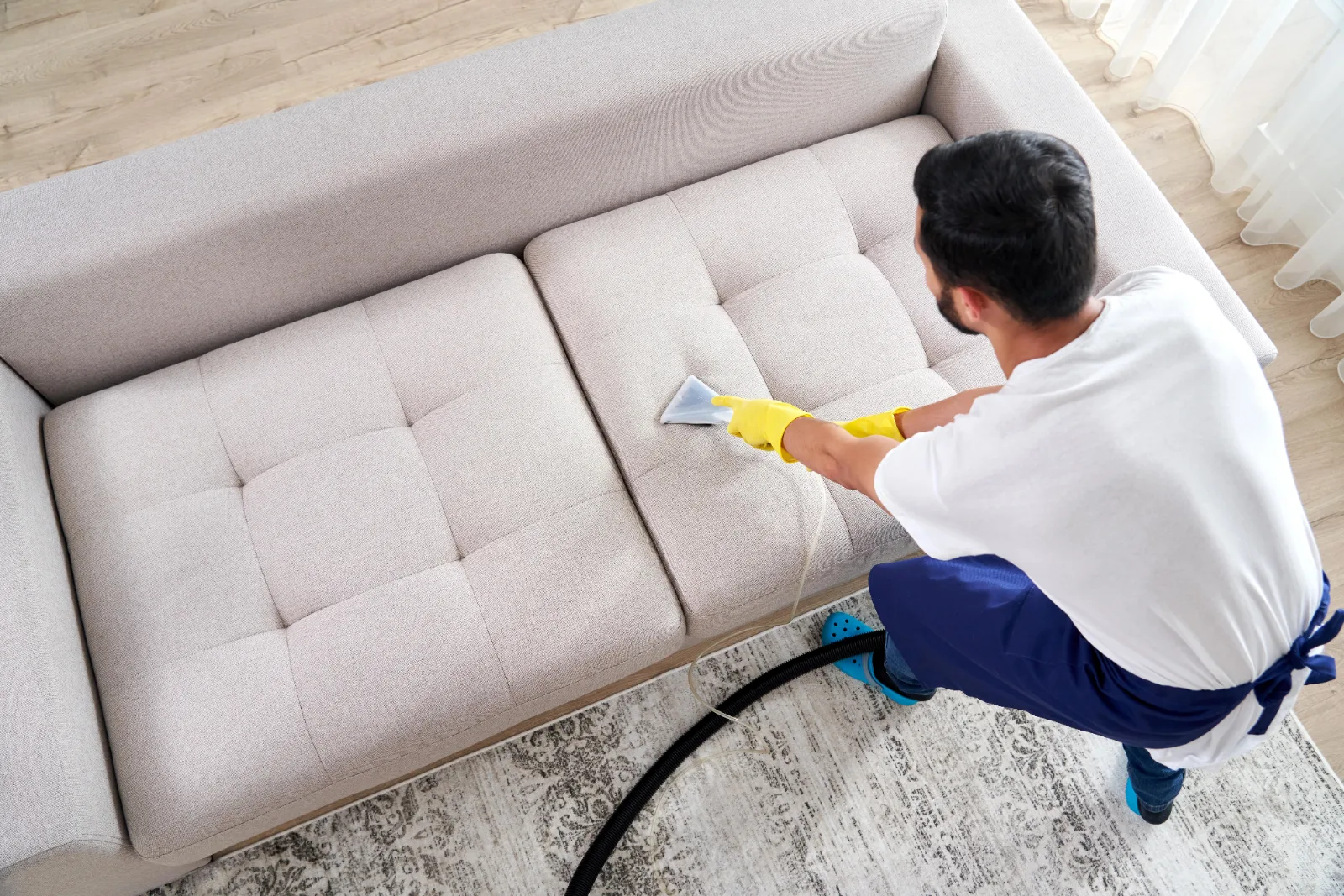 Technicien nettoyant un canapé en tissu clair avec une éponge